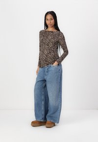 Leopard print long-sleeve top, high boat neck, paired with loose-fitting blue denim jeans and brown platform shoes, standing against a white background.