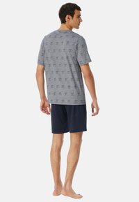 Grijze T-shirt met kort mouwen en een patroon, gecombineerd met marineblauwe shorts. Het shirt heeft een herhalend ontwerp over de stof.