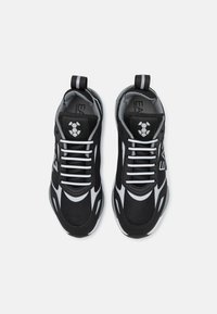 Mustat ja harmaat urheilukengät, joissa on verkkomateriaali, valkoiset yksityiskohdat ja litteät nauhat. Varustettu vetotakeilla ja logolla kielen kohdalla.