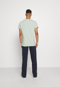 Ljusgrön t-shirt med korta ärmar, rund hals och avslappnad passform, kombinerad med mörkblå byxor. Enkel design, inga mönster eller dekorationer.