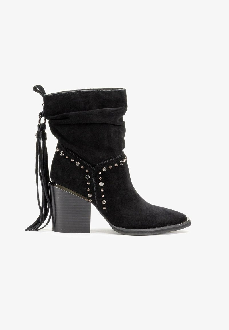 Botín negro de ante hasta el tobillo con parte superior arrugada, acentos de tachuelas y tacón cuadrado. Presenta un detalle de borlas en la parte trasera y un diseño de punta afilada.