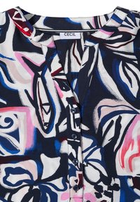 Kragen und Knopfleiste einer mehrfarbigen Bluse mit abstraktem Muster in Blau, Pink, Weiß und roten Pinselstrichen.