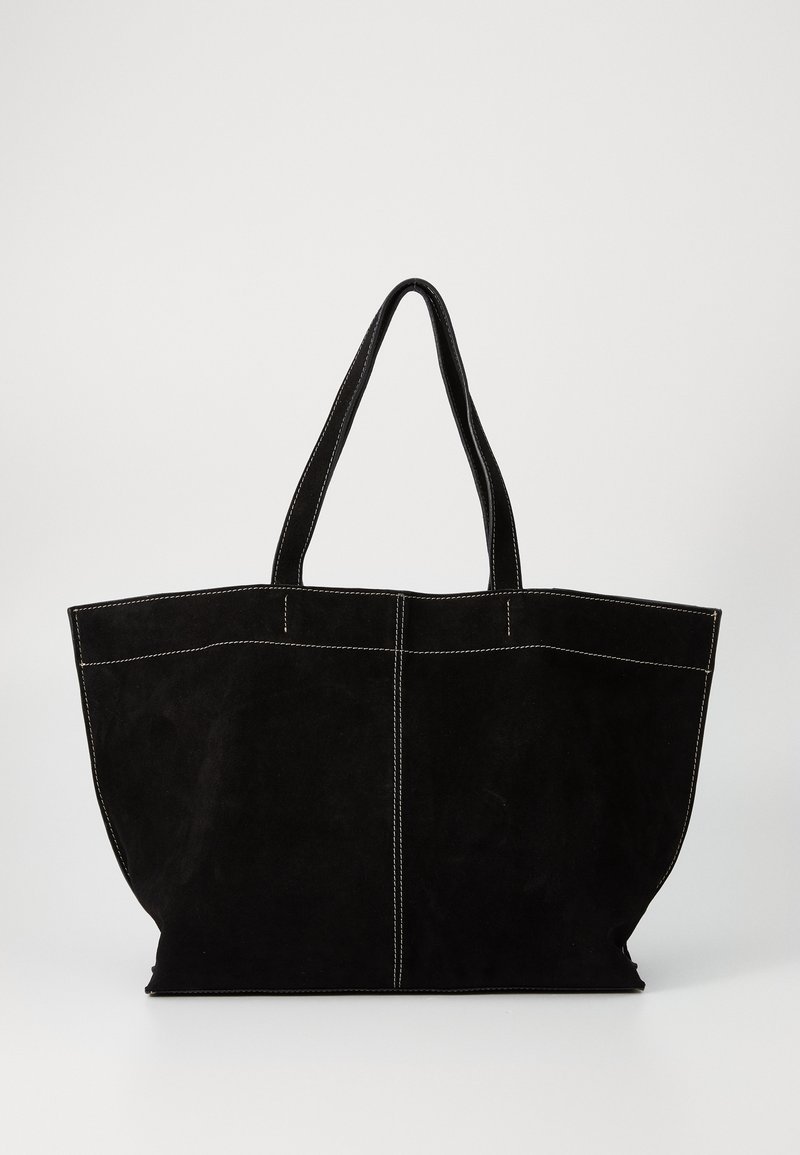 Sac cabas en daim noir avec des coutures blanches et deux bretelles, présenté sur un fond clair uni.