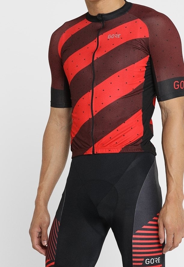 Jersey de ciclismo rojo y negro con rayas diagonales y patrones de puntos, con cremallera frontal y mangas cortas. Combinado con pantalones cortos de ciclismo acolchados negros.