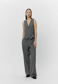 Gray, sleeveless vest with a deep V-neck and a fold-over design, paired with wide-leg gray trousers, featuring side pockets and smooth texture.