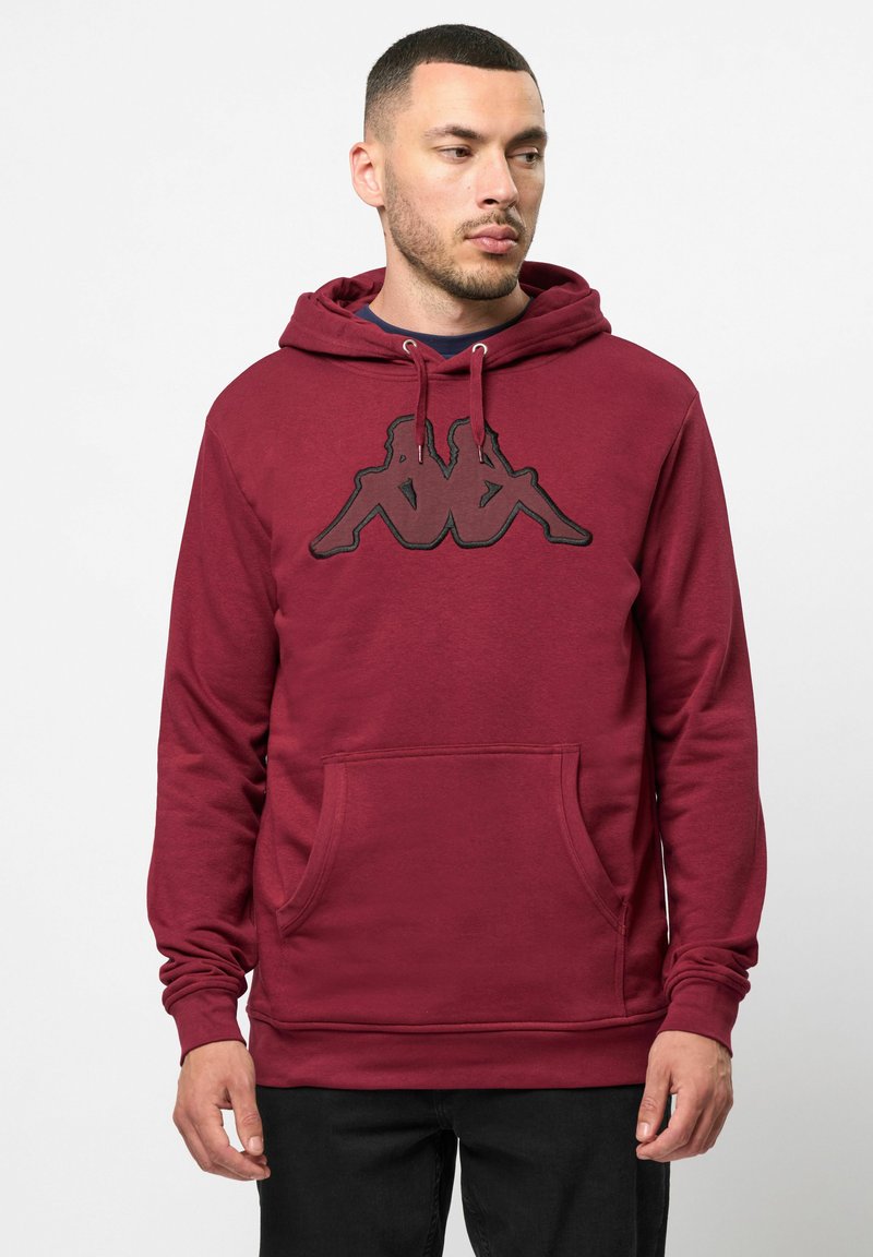 Bordová mikina s kapucňou a prednou klokankou, so stredovým čiernym grafickým logom. Mäkká tkanina s uvoľneným strihom.