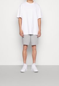 Bílé bavlněné tričko volného střihu, doplněné šedými bavlněnými šortkami po kolena. Celý outfit dotvářejí bílé vysoké tenisky.