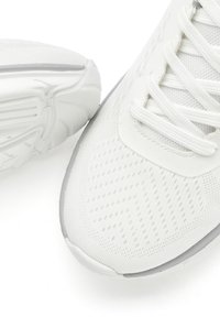 White athletic shoes with a mesh upper and textured design, featuring white laces, a smooth rubber sole, and gray accents on the outsole.