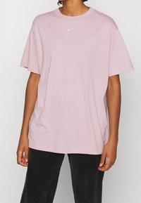 Ljusrosa bomullströja med korta ärmar, rund hals och en liten vit Nike-logga på bröstet. Matcherade med svarta manchesterbyxor.