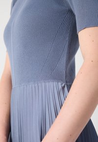 Pletené šaty ve světlé modrošedé barvě s žebrovaným horním dílem a sklady v dolní části. Mají krátké rukávy a přiléhavý korzet pro čistý siluetu.