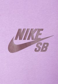 Nike SB-logga i en mörkbrun tryck på en ljuslila tygbakgrund. Designen har den ikoniska Nike-swooshen.