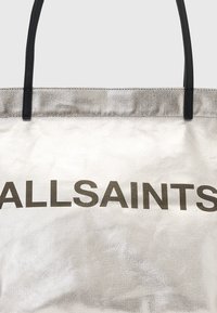 Borsa a spalla argento con finitura testurizzata, caratterizzata da una scritta nera in bold "ALLSAINTS". Include due manici neri per un facile trasporto.