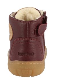 Stivale alla caviglia in pelle bordeaux con fodera beige morbida, zip laterale e fascetta in Velcro. Caratterizzato da una suola in gomma traslucida flessibile.
