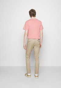 Krótka różowa bawełniana koszulka w połączeniu z beżowymi chinosami i brązowymi trampkami. Strój cechuje się luźnym krojem i minimalistycznym designem, bez wzorów.