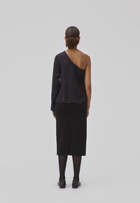 Asymmetrical black top with one long sleeve, textured fabric, and a fitted black skirt, ankle length, worn with black shoes.