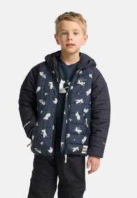 Vadderad jacka i marinblått med vita djurmönster, med dragkedja, huva och kontrasterande svarta ärmar. Buren över en mörk t-shirt.
