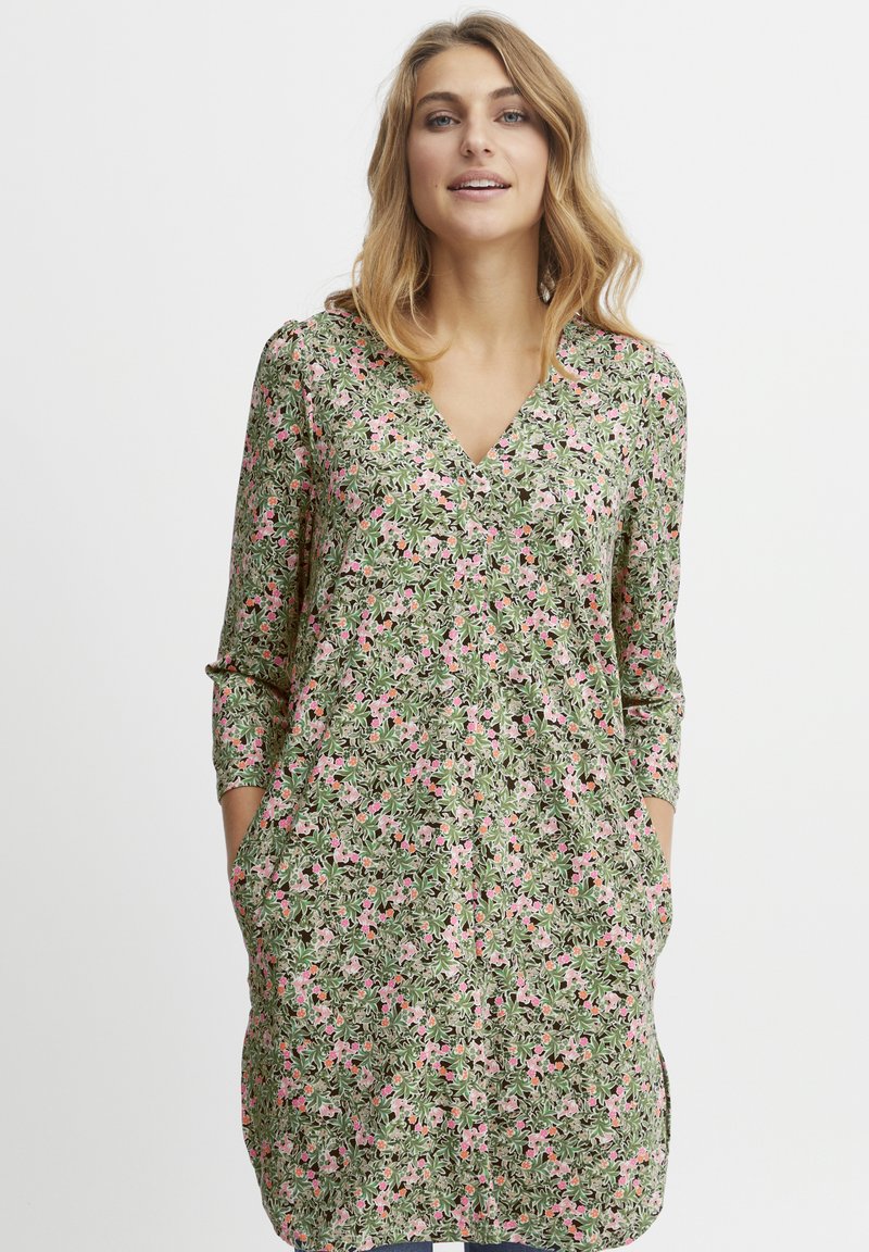Floral Kleid mit V-Ausschnitt, Dreiviertelärmeln und Taschen. Hat einen grünen Hintergrund mit rosa und weißen Blumenmustern.