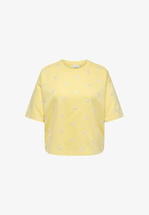 Dzeltena īsroku cropped T-krekls ar mazām baltām margrietiņu ziedu apdrukām, kas izkliedētas pa audumu.
