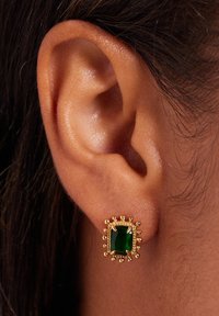 Groene rechthoekige edelsteen oorbellen gezet in goud, met een gestructureerde rand en ronde accenten, gedragen aan de oorlel tegen donker haar.
