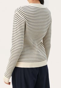 Maglione lavorato a maglia color crema con motivo a griglia blu navy, design aderente, scollo rotondo, polsini e orlo a coste. Superficie texture per maggiore profondità.