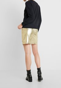Sudadera negra, falda mini metálica dorada con textura arrugada y botines negros con cremallera y detalle de hardware circular.