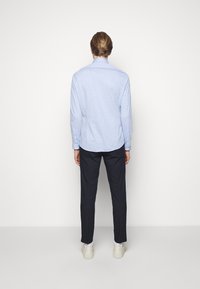 Camicia azzurro chiaro a maniche lunghe, con orlo arrotondato, abbinata a pantaloni scuri e sneakers bianche. Tessuto liscio, dettagli con polsini abbottonati.