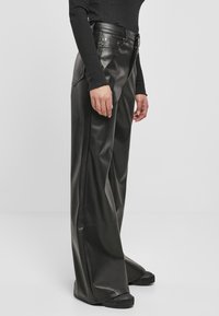 Čierne kožené nohavice so širokými nohavicami, vysokým pásom, prednými vreckami a tonálnym prešívaním. Hladká textúra a jemný lesk.
