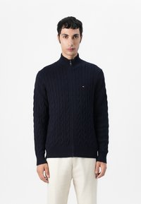 Navy blå glidelås cardigan laget av teksturert strikk med kabelmønster, med ståkrage og ribbestrikkede mansjetter og hem.