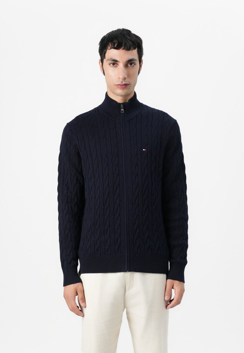 Navy blå glidelås cardigan laget av teksturert strikk med kabelmønster, med ståkrage og ribbestrikkede mansjetter og hem.