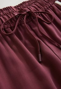 Shorts en tissu bordeaux avec une taille élastique froncée, dotés d'un cordon de serrage noué et d'une texture lisse.