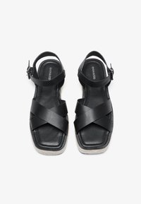 Svarte sandaler med kryssrem-design, laget av glatt lær. Har en flat såle med teksturert kanting og en justerbar ankelrem.