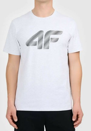 Mężczyzna w jasnoszarej koszulce z czarnym, teksturowanym logo "4F" z przodu, ubrany w czarne spodnie na jednolitym tle.