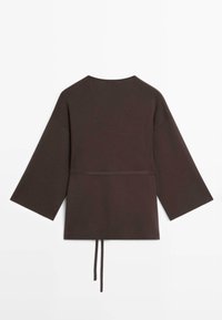 Donkerbruin langärmelig bovenstuk met brede mouwen, ronde halslijn en een dunne tailleband die aan de achterkant hangt, plat gelegd op een witte achtergrond.