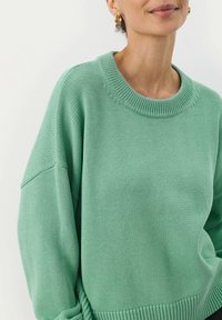Pull en vert menthe avec un col rond à côtes, des épaules tombantes et un motif en maille texturé. Matière douce avec une coupe décontractée.