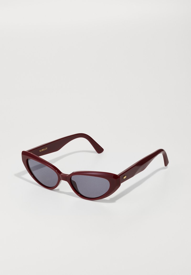 Lunettes de soleil en plastique bordeaux en forme d'œil de chat avec des verres gris. Présentent une finition lisse et un logo doré subtil sur les branches.
