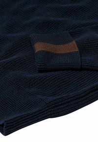 Marineblaue gestrickte Textilie mit einem horizontalen braunen Streifen. Das Material hat eine strukturierte Oberfläche mit gerippten Details, die visuelle Tiefe erzeugen.