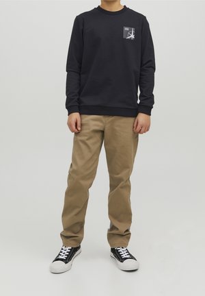 Sweat-shirt bleu marine avec un petit motif dans la zone de la poche poitrine, associé à un pantalon kaki et des baskets noires avec embouts blancs. Design et coupe simples.