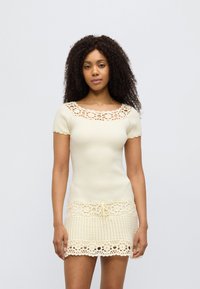 Εκρού ριμπ πλεκτό τοπ με κοντά μανίκια και τετράγωνη λαιμόκοψη, συνδυασμένο με δαντελωτό κέντημα στο κάτω μέρος και κορδόνι στη μέση.