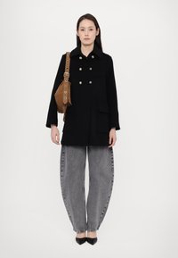 Black double-breasted coat with gold buttons, two front pockets, paired with oversized grey denim pants and black pointed-toe heels.