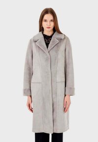 Cappotto lungo grigio chiaro realizzato in materiale morbido, con collarino a punte, tasche laterali e una silhouette dritta con dettagli di cucitura visibili.