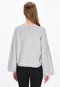 Szary sweter z długimi, szerokimi rękawami i krojem w stylu cropped. Materiał wydaje się miękki i dziany, z delikatną teksturą i surowym wykończeniem.