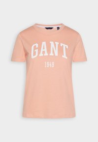Jasnopomarańczowa koszulka z krótkim rękawem, z białym napisem "GANT" i datą "1949" wydrukowaną poniżej z przodu.