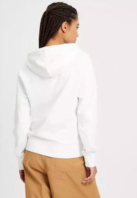 Biała bluza z kapturem o płaskim kroju, z regulowanym kapturem i ściągaczami przy mankietach. W połączeniu z beżowymi spodniami typu cargo. Gładka tekstura i prosty design.