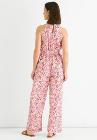 Floral jumpsuit in soft fabric, featuring a pink, red, and white pattern, halter neck design, wide legs, and a keyhole back detail.