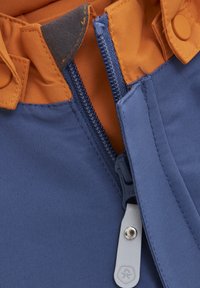 Blått tyg med en orange foder, med en central dragkedja, tryckknappsförslutning och en grå dragkedjehandtag. Texturen verkar slät och hållbar.