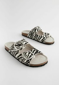 Sorte og hvide zebra mønster sandaler med to justerbare sølvspænder, blød suede-lignende overdel og en tekstureret sort sål.