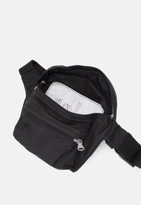 Schwarze Nylon-Crossbody-Tasche mit einem Hauptfach mit Reißverschluss und einer Vordertasche. Verfügt über einen strukturierten Gurt und ein Innenetikett mit Pflegehinweisen.