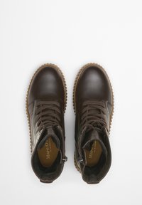 Bottes dcuir brun montant jusqucheville avec cts texturs, bouts ronds et semelles en caoutchouc. Elles sont dotes de lacets et de fermetures glissires sur le ct pour la fermeture.