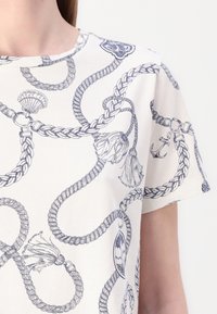 Bomulds T-shirt med hvid bund og blå nautisk reb- og ankerprint, korte ærmer og rund halsudskæring.