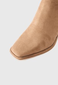 Tan suede ankle boot with a square toe and a smooth texture, featuring a minimalistic design and a subtle stitched edge.